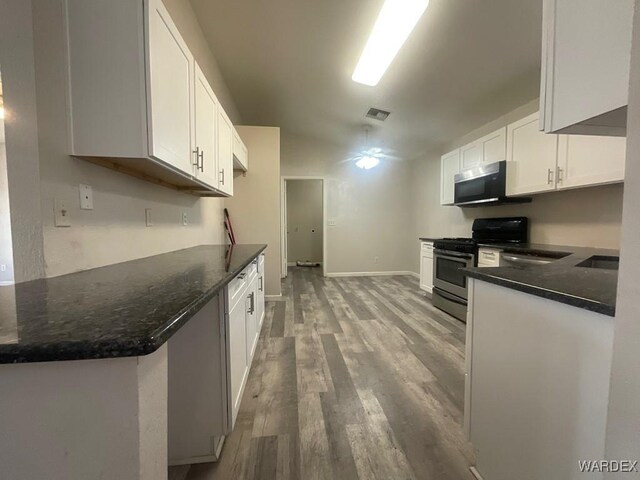 kitchen with appliances with stainless steel finishes, light wood-style floors, white cabinetry, a peninsula, and baseboards