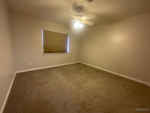 empty room featuring ceiling fan, dark carpet, and baseboards