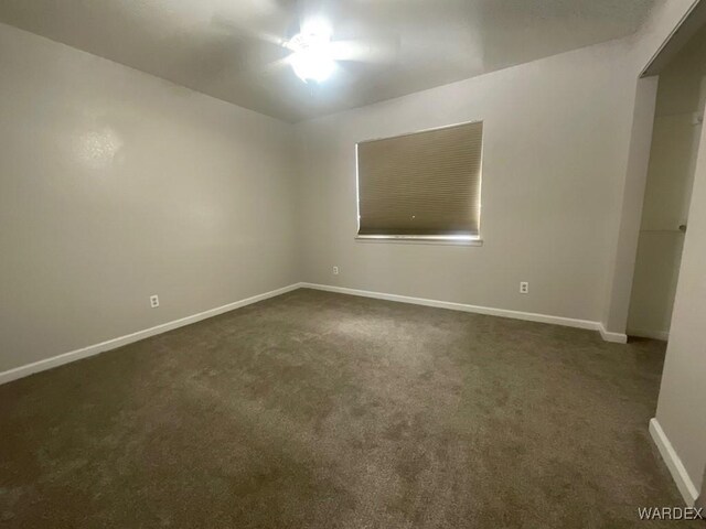 empty room featuring dark colored carpet and baseboards