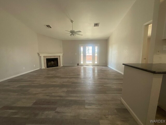 unfurnished living room featuring baseboards, visible vents, a tiled fireplace, ceiling fan, and dark wood-style flooring