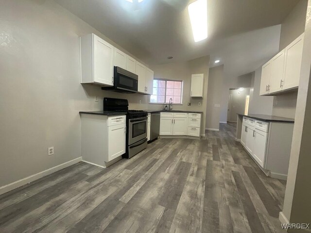 kitchen with dark wood-type flooring, white cabinetry, baseboards, appliances with stainless steel finishes, and dark countertops