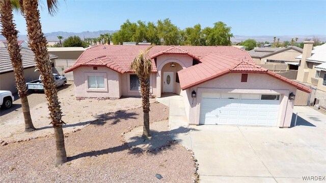 mediterranean / spanish home with an attached garage, a mountain view, driveway, a tiled roof, and stucco siding