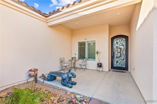 view of exterior entry featuring a patio area, a tile roof, and stucco siding