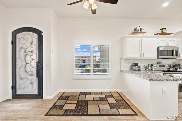 kitchen featuring baseboards, a peninsula, light stone countertops, stainless steel appliances, and white cabinetry