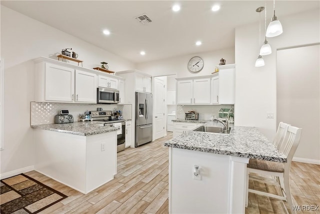 kitchen with a peninsula, appliances with stainless steel finishes, white cabinets, and a sink