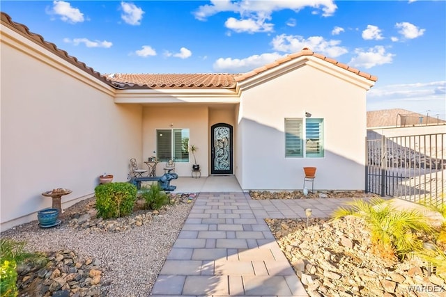 entrance to property featuring a patio area, a tile roof, fence, and stucco siding