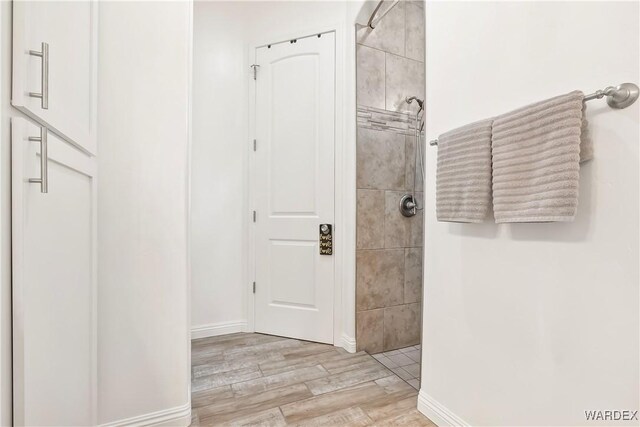 bathroom with a tile shower, baseboards, and wood finished floors