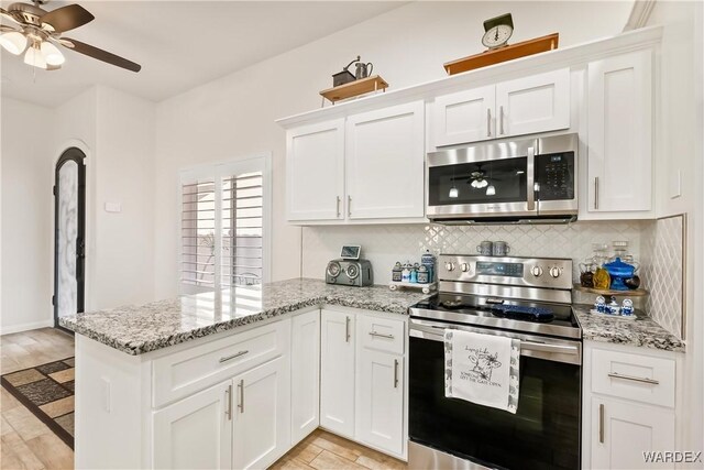 kitchen with white cabinets, light stone counters, stainless steel appliances, and backsplash