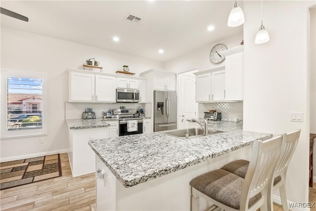 kitchen with a peninsula, white cabinets, stainless steel appliances, and a sink