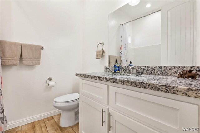 bathroom with curtained shower, toilet, vanity, wood finished floors, and baseboards