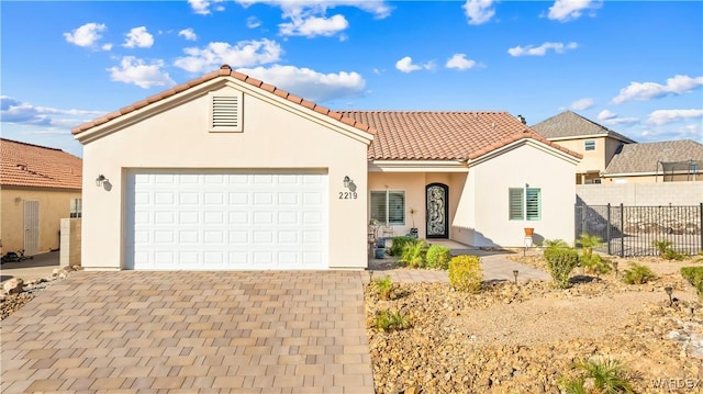 mediterranean / spanish-style home featuring a garage, a tile roof, fence, decorative driveway, and stucco siding