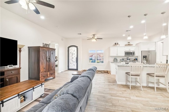 living area with light wood-style floors, arched walkways, ceiling fan, and recessed lighting