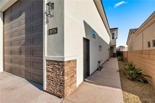 view of side of property featuring a garage, stone siding, fence, and stucco siding