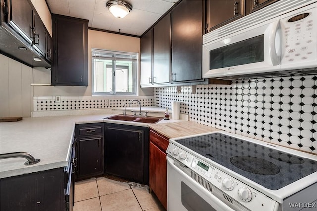 kitchen with a sink, white appliances, light countertops, light tile patterned floors, and decorative backsplash