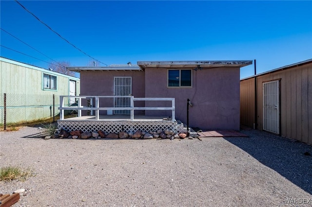 rear view of house featuring stucco siding, a deck, and fence