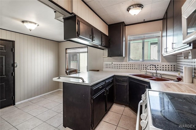 kitchen featuring a sink, electric range oven, a peninsula, light tile patterned flooring, and light countertops