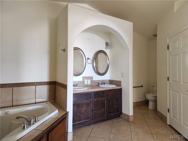 full bath with tile patterned flooring, a garden tub, a sink, and toilet