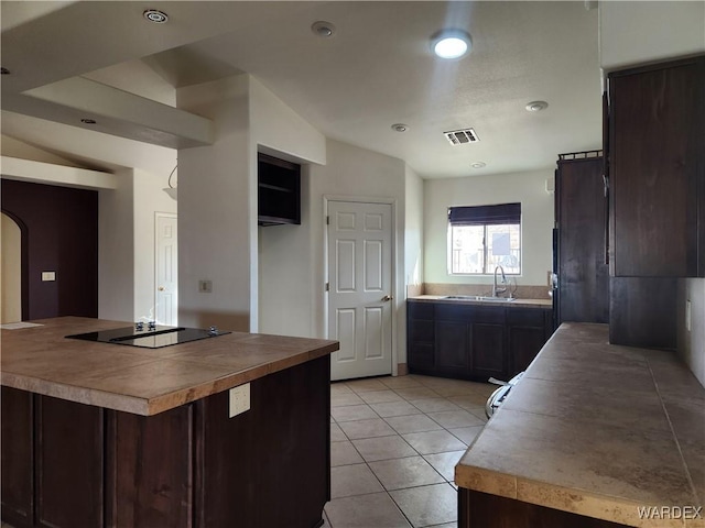 kitchen featuring arched walkways, light tile patterned flooring, dark brown cabinetry, a sink, and visible vents