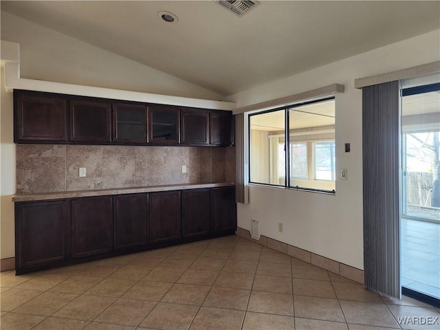 kitchen featuring dark brown cabinetry, visible vents, vaulted ceiling, light countertops, and backsplash