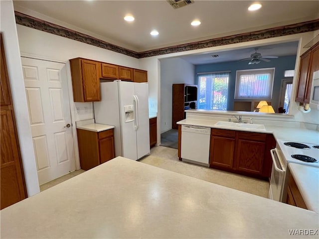 kitchen with brown cabinets, light countertops, visible vents, a sink, and white appliances