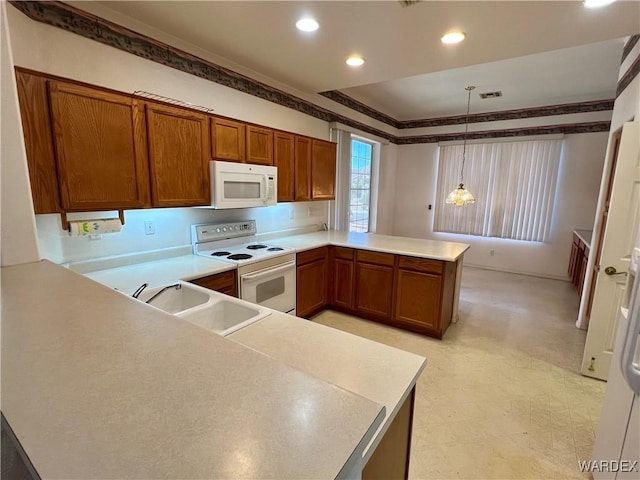 kitchen featuring a peninsula, white appliances, a sink, light countertops, and decorative light fixtures