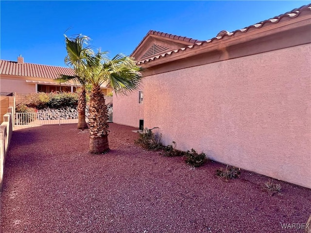 view of side of property with fence, a tiled roof, and stucco siding