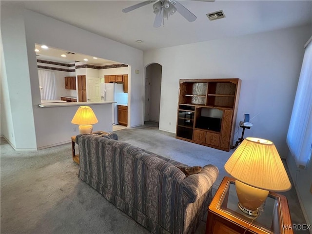 living area with arched walkways, baseboards, visible vents, and light colored carpet