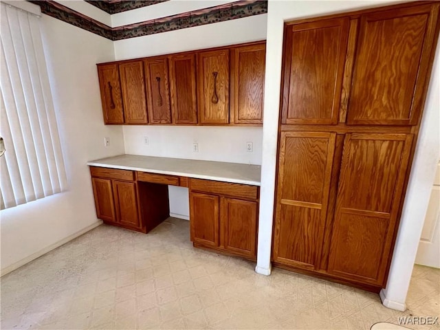 kitchen with built in desk, light floors, light countertops, brown cabinetry, and baseboards