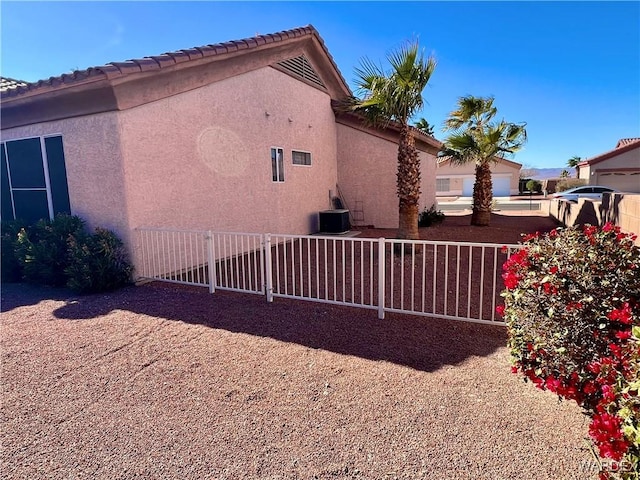 view of side of property featuring central AC, fence, and stucco siding