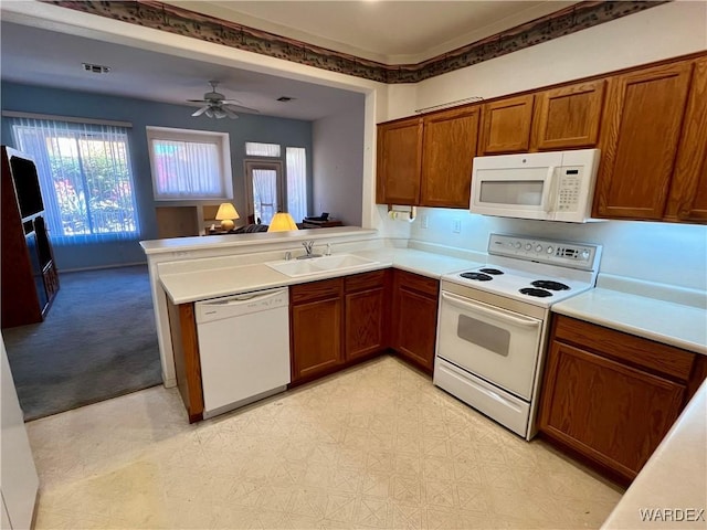 kitchen featuring light countertops, open floor plan, a sink, white appliances, and a peninsula