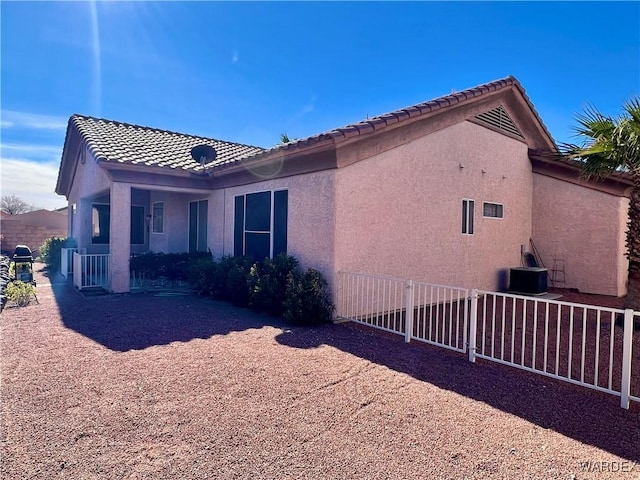 view of side of property with a tile roof, fence, central AC, and stucco siding