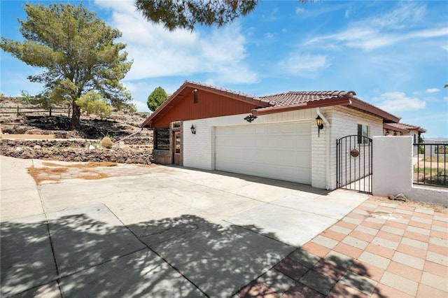 898 Crestwood Ln, Kingman, AZ 86409 - view of side of home featuring brick siding, concrete driveway, a tile roof, an attached garage, and a gate