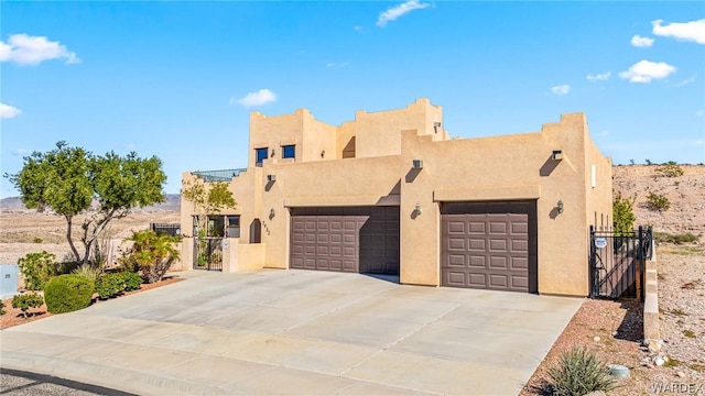 pueblo-style home with concrete driveway, fence, an attached garage, and stucco siding