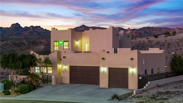 pueblo-style house featuring driveway, fence, a mountain view, and stucco siding