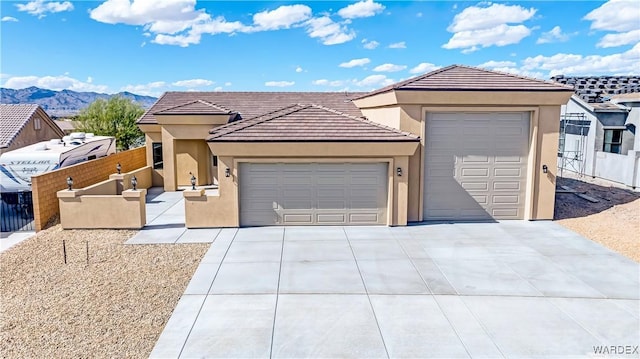 view of front of home with a garage, driveway, fence, a mountain view, and stucco siding