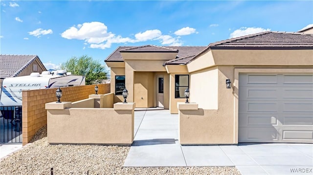 view of front facade with an attached garage, fence private yard, a tile roof, and stucco siding