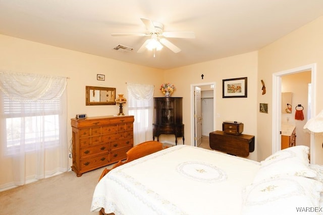 bedroom featuring visible vents, light colored carpet, ceiling fan, ensuite bathroom, and a spacious closet