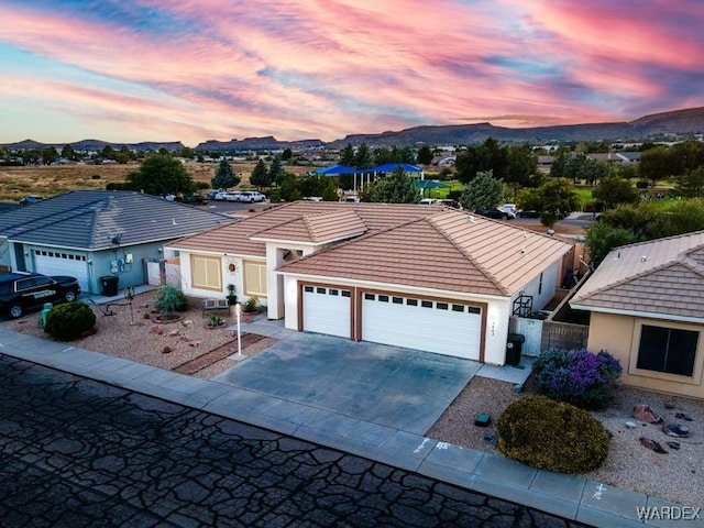 view of front facade with an attached garage, a mountain view, a tile roof, concrete driveway, and stucco siding