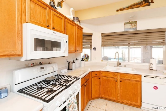 kitchen featuring brown cabinets, light tile patterned floors, light countertops, a sink, and white appliances