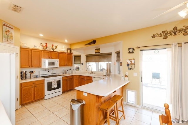 kitchen with white appliances, visible vents, a breakfast bar area, a peninsula, and light countertops