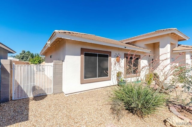 rear view of property featuring fence, a gate, and stucco siding