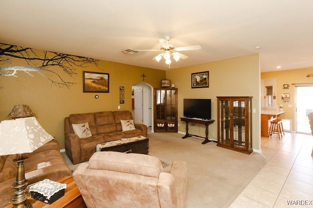 living area with arched walkways, light tile patterned floors, light carpet, visible vents, and a ceiling fan