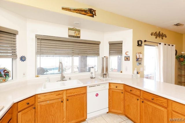 kitchen with light tile patterned floors, light countertops, visible vents, white dishwasher, and a sink