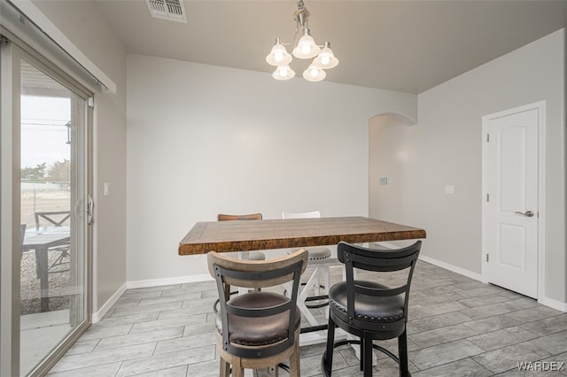 dining area with visible vents, baseboards, wood tiled floor, a chandelier, and arched walkways