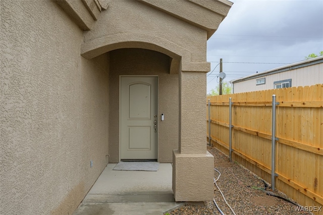 doorway to property with stucco siding and fence