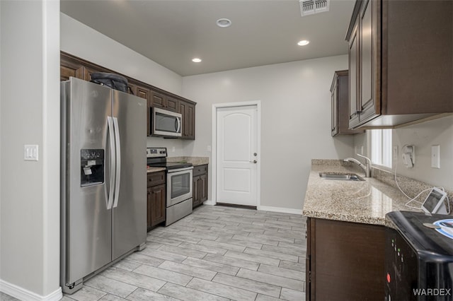 kitchen with light stone counters, visible vents, a sink, dark brown cabinetry, and appliances with stainless steel finishes