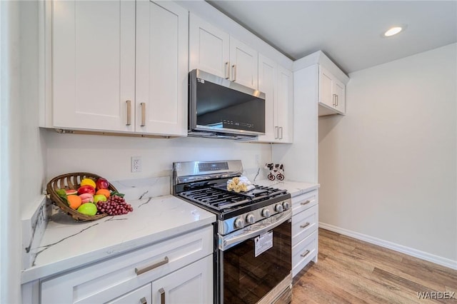 kitchen with light stone counters, baseboards, light wood-style floors, appliances with stainless steel finishes, and white cabinetry