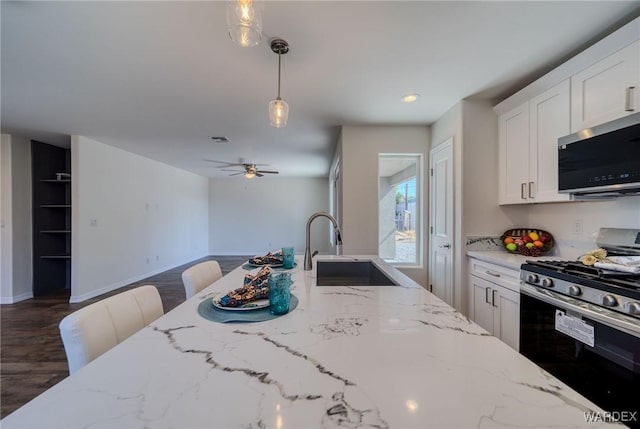 kitchen with a sink, stainless steel appliances, light stone countertops, and decorative light fixtures