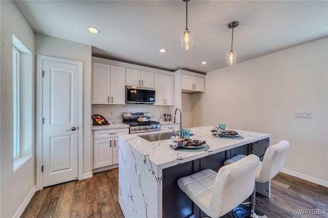 kitchen with a sink, dark wood finished floors, stainless steel appliances, white cabinets, and hanging light fixtures