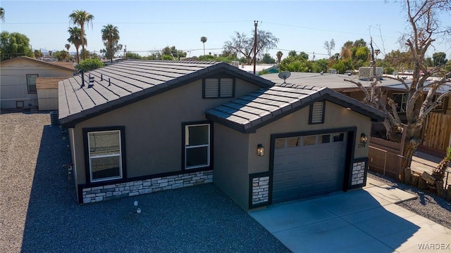 view of front of home featuring fence, concrete driveway, a garage, stone siding, and a tile roof